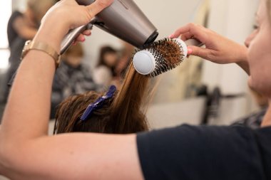 Yetenekli bir stilist şık bir kuaförde saç kurutma makinesi ve yuvarlak fırça kullanır.