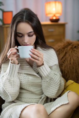 Saf rahatlık ve rahatlık için ideal bir oturma odası ortamında huzur içinde çay yudumlayan bir kadın.