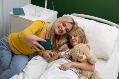 Gönüllü bir selfie, umut dolu bir hastane odasında sevgi dolu bir anne ve kızı neşeli bir anı paylaşırken yakalar.