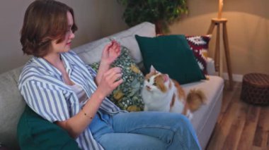 Bir insan hoş ve rahatlatıcı bir anın tadını çıkarır. Keyifle tatlı bir kediyle kanepede oynar.