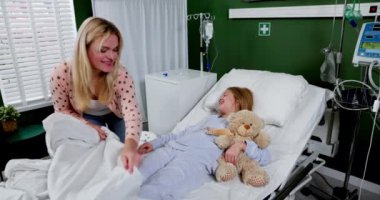 Yürek ısıtan bir hastane sahnesinde, kendini adamış bir bakıcı hasta bir çocuğu elinde oyuncak ayıyla nazikçe rahatlatır.