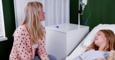 İki genç kız kardeş, sıcak bir hastane odasında birbirlerine ilgi ve ilgi göstererek destekleyici bir anı paylaşıyorlar.