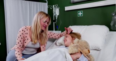 Yetiştiren bir anne, hasta çocuğunu bir hastane yatağında rahat ettirir. Derin bir sevgi ve sarsılmaz bir destek gösterir.