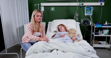 Kendini adamış bir anne, hasta çocuğunu bir hastane odasında sevgiyle rahatlatıyor, derin bir sevgi ve destek gösteriyor.