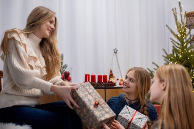 Üç yakın arkadaş, güzel dekore edilmiş Noel ağacının oradaki şenlikli bir ortamda birbirlerine düşünceli hediyeler veriyorlar.