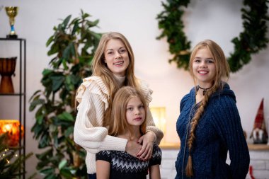 Üç kız kardeş mutlu bir şekilde rahat ve rahat bir şekilde poz veriyorlar, hepsi de neşeli bir arkaplanda.