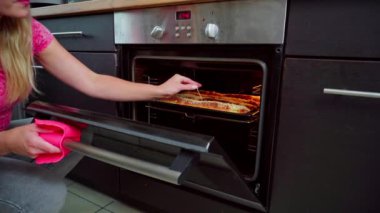 Bir kadın şık bir mutfakta lezzetli yemeklerini dikkatlice fırından çıkarmak için canlı pembe bir havlu kullanıyor.