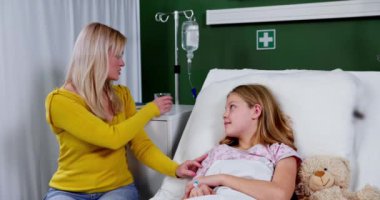 Bir anne, hasta kızını sevgiyle bir hastane odasında destekleyip sıcak ve umut dolu bir atmosfer yaratır..