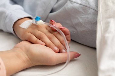 Yürekten bir hastane ziyareti sırasında sevgi ve desteği simgeleyen sevdiklerimizin ellerinin birbirine dolandığı dokunaklı bir sahne.