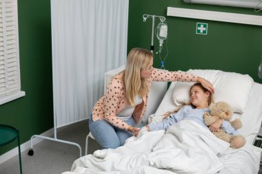 Sadık ve ilgili bir anne, hasta çocuğuna hastanede birlikte yatarken güvence veriyor.