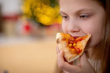 Saf mutlulukla dolu lezzetli bir dilim pizzanın tadını çıkaran neşeli, genç bir çocuk.