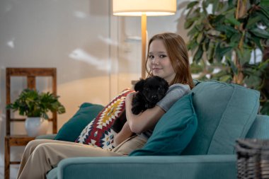 Şık ve sakin bir oturma odası ortamında, genç bir kız sevgili evcil hayvanıyla sarılıp, konforun keyfini çıkarıyor.