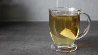 Aromatik bitkisel çayla dolu berrak bir cam bardak, canlı rengini sergiliyor ve dingin bir ortam yaratıyor.