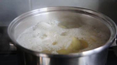 Mutfak sahnesinde kaynayan sıcak suyla çevrili bir tencerede kaynayan patates parçaları.