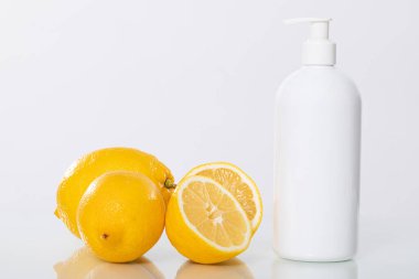 Modern bir losyon şişesinin yanına yerleştirilmiş canlı sarı limonlar, taze narenciye teması için ideal.