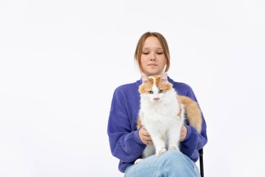 Güzel bir minimalist stüdyo ortamında, genç bir kadın tüylü turuncu ve beyaz kedisiyle neşe içinde poz verir.