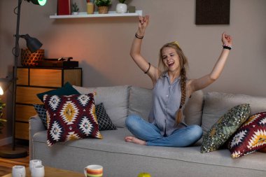 Neşeli bir kadın, rahat, keyifli bir ortamda renkli yastıklarla çevrili kanepede vakit geçirmekten zevk alır.