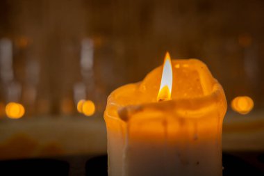 Yanıp sönen bir mum alevinin yakın çekimi, yumuşak bokeh ışıklarıyla ılık bir ortam yaratarak havayı canlandırır.