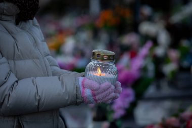 Bir insan, güzel bir çiçeğin ortasında mum tutuyor. Anma ve onuru yansıtıyor.