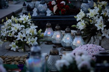 Canlı çiçeklerle ve mezarın üzerinde parlayan fenerlerle dolu sakin bir sahne merhum için derin anıları sembolize ediyor.