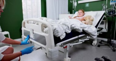 Kendini adamış bir hemşire hastane yatağında oyuncak ayıyla bir çocuğa bakıyor. Derin bir şefkat ve rahatlık gösteriyor.