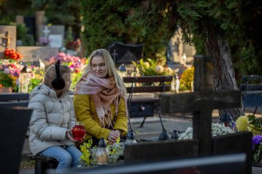 İki insan huzurlu bir mezarlıkta güzel çiçeklerle süslenmiş, kayıp sevdiklerini onurlandıran bir anı paylaşıyor.