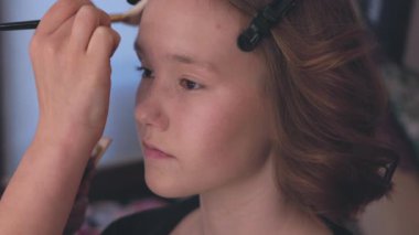 Genç bir kız şık bir kuaförde keyifli bir makyaj seansından zevk alıyor, güncel güzellik eğilimlerini kucaklıyor.