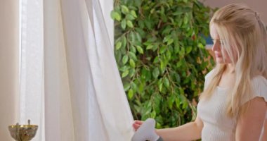 Genç bir kadın şık, modern ev ortamında havadar perdeleri ustalıkla kendi ışığına buharlı kumaş kullanıyor.