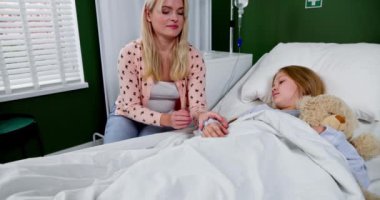 Huzurlu bir hastane odasında, şefkatli bir anne hasta çocuğunu rahatlatır, yumuşak bir oyuncak ayıyı yanında tutar.