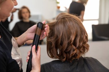 Yetenekli bir stilist, şık bir kuaförde müşterinin saçında çarpıcı kıvrımlar yaratır.