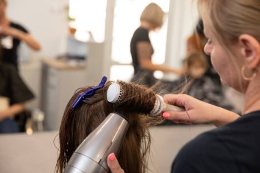 Son derece yetenekli bir stilist saçlarını ustalıkla üflüyor. Parlak ve parlak bir son elde etmek için yuvarlak bir fırça kullanıyor.