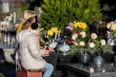 Two individuals reflect on their loved ones among vibrant flowers in a serene cemetery, filled with memories clipart