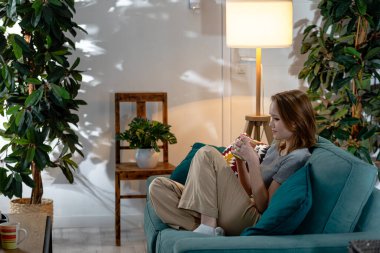 Salonda sakin bir atmosfer, güzel bitkilerle çevrili bir kanepede rahatça oturan bir insanı gösteriyor.