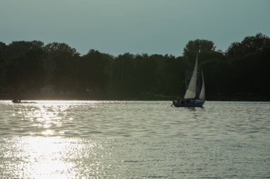 Işıldayan göl sularının üzerinde alacakaranlığın büyüleyici ve huzurlu güzelliğini yakalayan sakin bir yelken sahnesi.