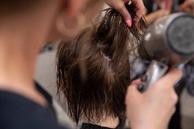 Yetenekli bir stilist, şık bir kuaför ortamında zarif ve şık bir saç stili yaratmak için saç kurutma makinesi kullanır.