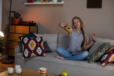 Bir kadın rahat bir şekilde rahat bir kanepede oturuyor ve güzel oturma odasının sıcak atmosferinin tadını çıkarıyor.