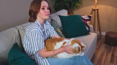 Genç bir insan, şık, rahat bir oturma odasında pofuduk, sevecen bir kediyle huzurlu bir anın tadını çıkarır.