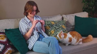 Kanepesinde dinlenirken bir kadının kedisiyle sevgiyle etkileşime geçtiği rahat bir oturma odası.