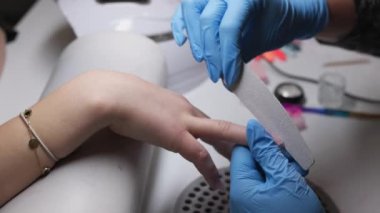 Yetenekli ve profesyonel bir tırnak teknisyeni manikür seansı sırasında bir dosyayla tırnakları ustalıkla şekillendiriyor ve inceliyor.