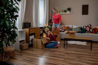 Arkadaşlar, sıcak ışıkla dolu şık bir oturma odasında, neşeli ve rahat bir ortam yaratarak, kutuları açmaktan mutluluk duyarlar.