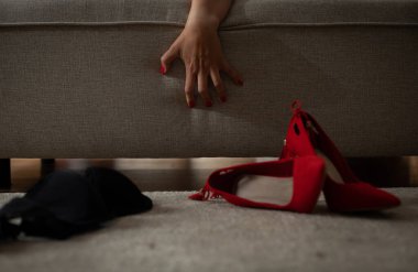 Zarif bir el zarif bir şekilde rahat bir kanepenin arkasından uzanır, şık kırmızı topuklu ayakkabılara yakın bir yerde.