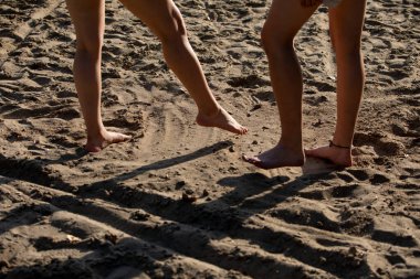İki çift küçük ayak neşeyle dans ediyor ve sıcak, kumlu arazide oynuyor. Saf hareket ve mutluluk sergiliyor.