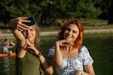 Nehir kenarında güneşli bir günün tadını çıkaran iki genç kadın neşeli bir selfie ile neşeli anılarını yakalıyorlar.