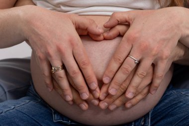 Bir çift elleri hamile karnında bir kalp oluşturur. Sevinçle yeni bir hayatı kutlarlar.