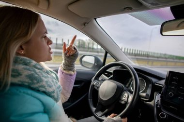 Yoğun bir otoyolda araba sürerken, tasasız tavrını ve modern yaşam tarzını sergileyen bir kadın kendinden emin bir şekilde el kol hareketi yapar.