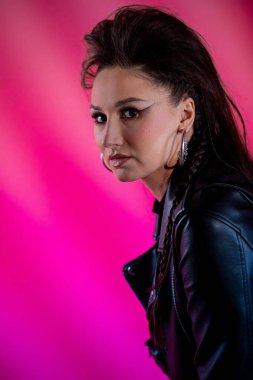 Zarif bir deri ceket giyen kendine güvenen bir kadının çarpıcı ve cesur portresi canlı pembe bir arka plana karşı.