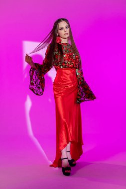 Göz kamaştırıcı bir model, parlak pembe bir ortamda, çarpıcı kırmızı bir elbise ve karmaşık detaylar sergiliyor..
