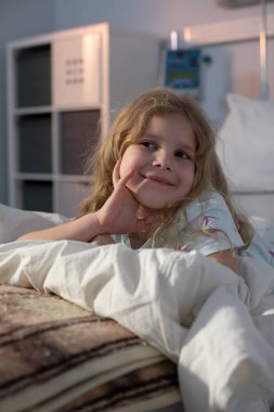 Neşeli bir kız, sıcak bir ortamda, rahat bir yatakta, neşe ve merak saçarak rahatlıyor.