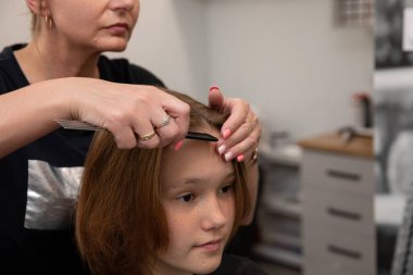 Çağdaş bir salon ortamında, yetenekli bir stilist genç bir müşterinin saçını dikkatlice kesiyor.