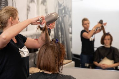 Uzman bir kuaför, müşterisinin saçı üzerinde özenle çalışıyor. Modern, lüks bir kuaför salonu ortamında.